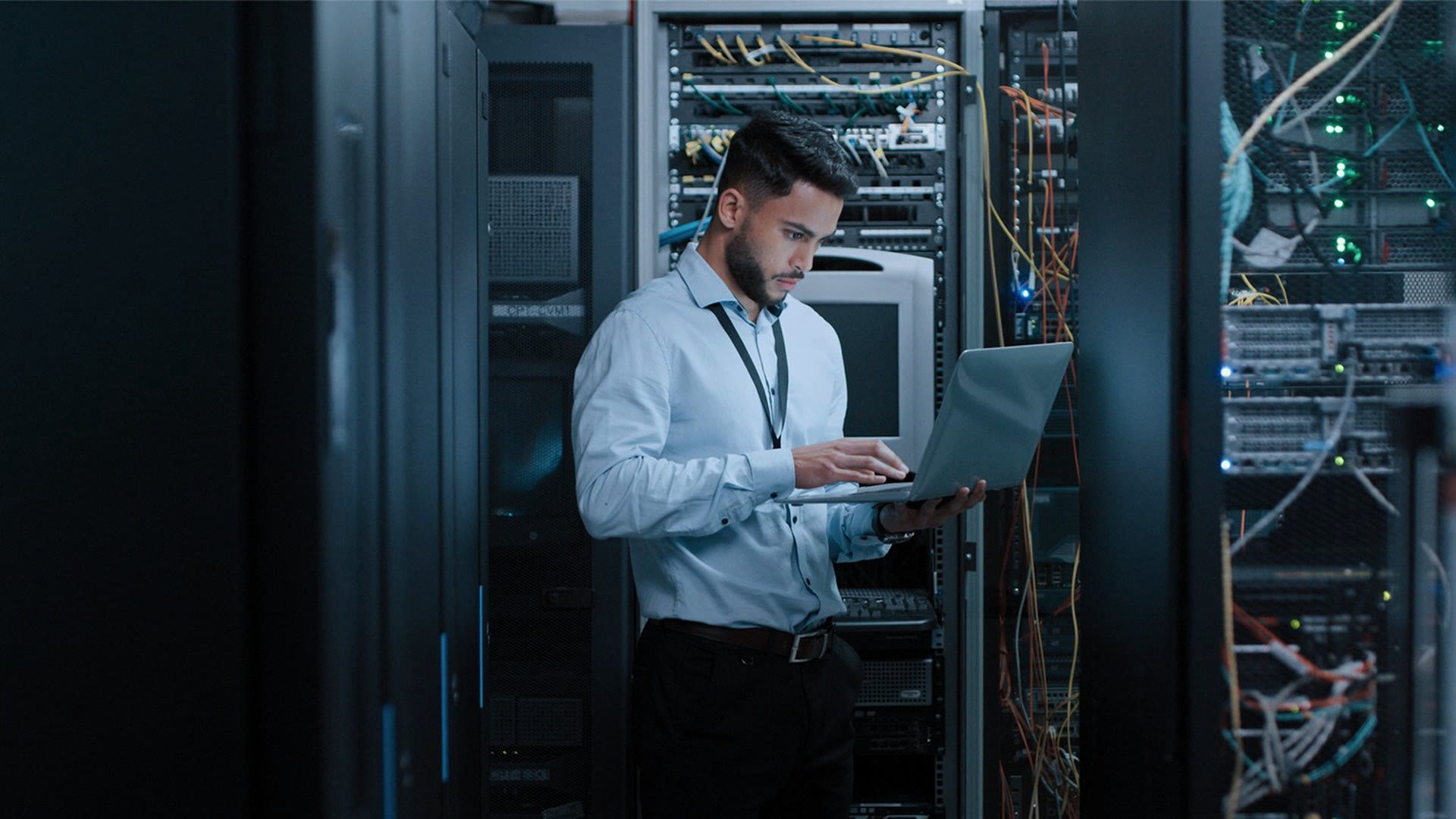 Stand-in footage: an engineer holds a laptop in front of an open rack in a data centre aisle.